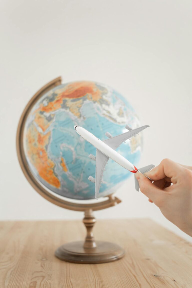 Close-up of a hand with a toy airplane in front of a globe, symbolizing travel and exploration.